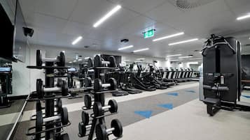 Un gimnasio con diversos equipos de ejercicio, incluyendo cintas de correr y máquinas de pesas, organizados en filas.