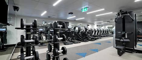 Une salle de sport équipée de divers appareils d’exercice, notamment des tapis de course et des appareils de musculation, disposés en rangées.