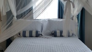 Una cama con dosel, almohadas y una ventana con cortinas.