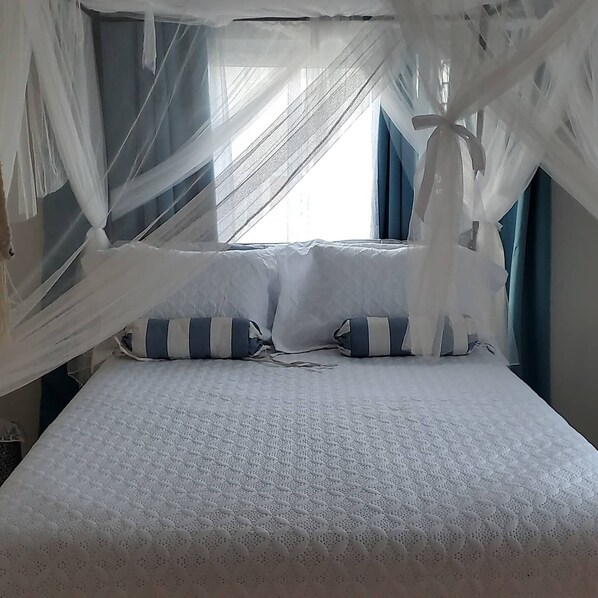 A bed with a white quilt, blue and white striped pillows, and white canopy drapes.