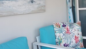 Una habitación con dos sillas turquesas, una pared blanca, un adorno con forma de brújula y un cuadro de una playa.