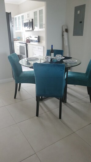 A dining area with a round glass table, teal upholstered chairs, and a white cabinet in the background.