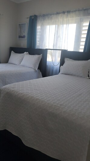 A hotel room with two beds, a window with curtains, and a painting on the wall.