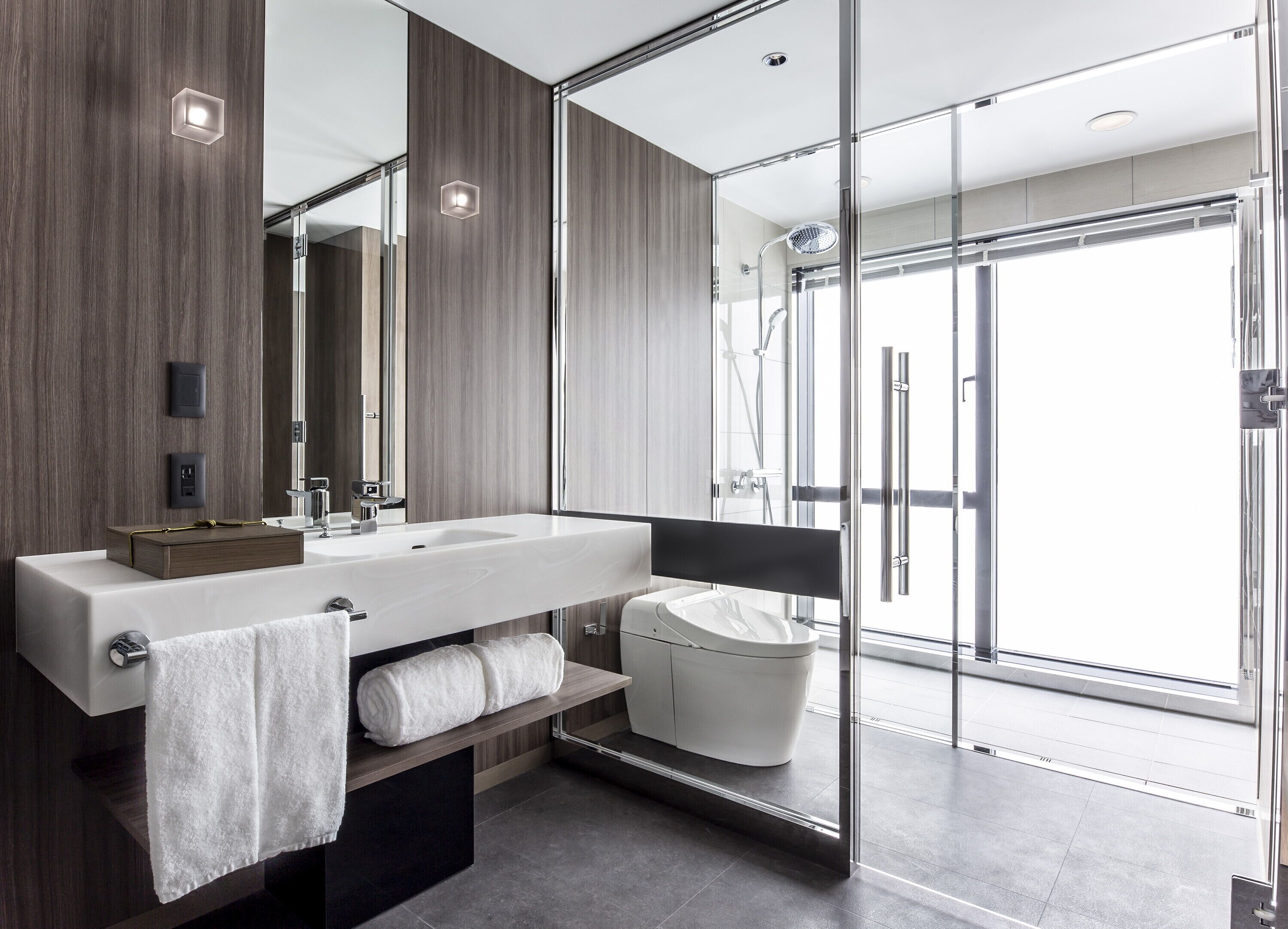 A modern bathroom with a large mirror, a wooden vanity, a glass shower enclosure, and a toilet.