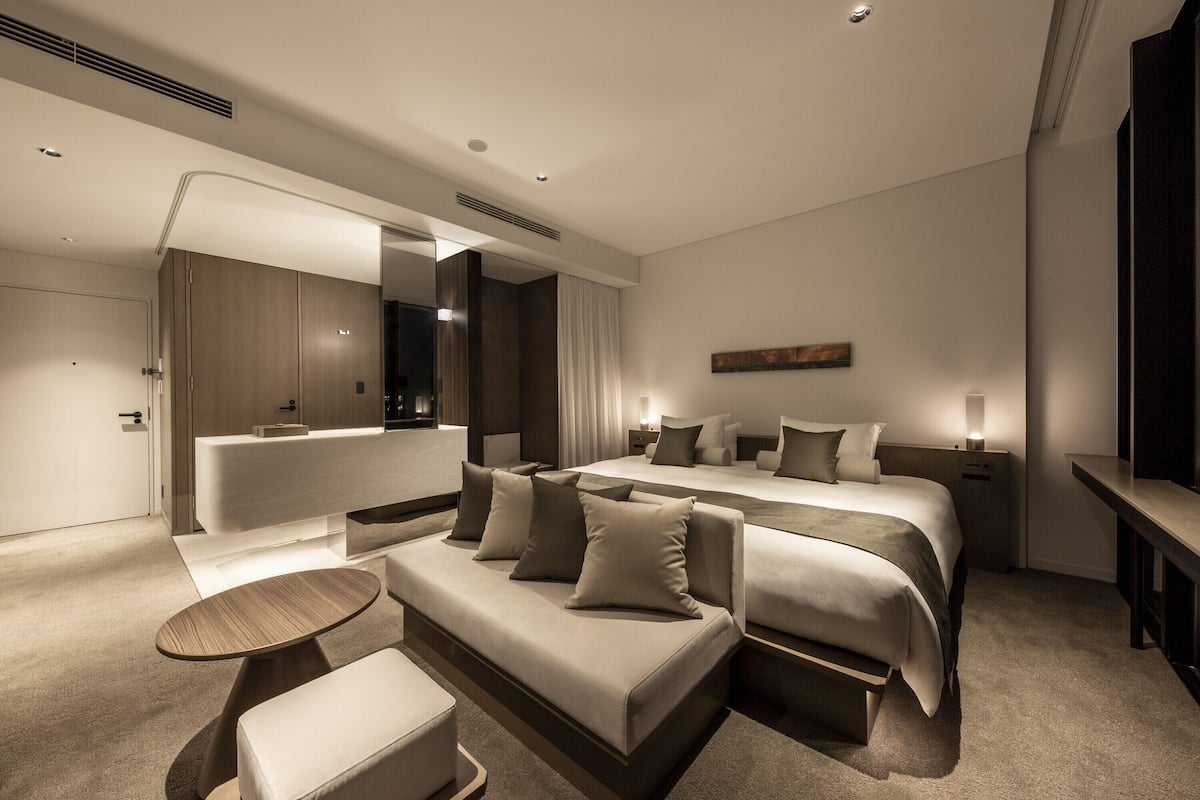 A modern hotel room with a large bed, a sofa, a small table, and a mirror.
