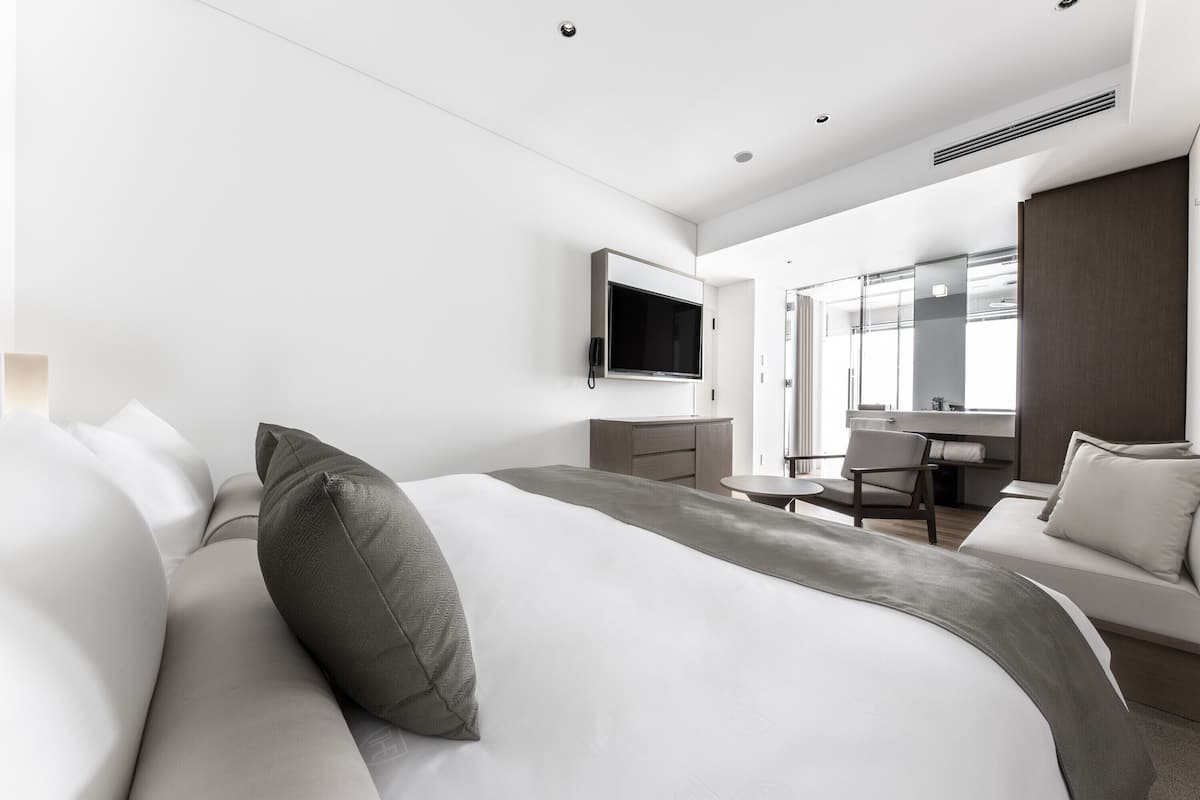 A modern hotel room with a large bed, a desk, and a TV mounted on the wall.