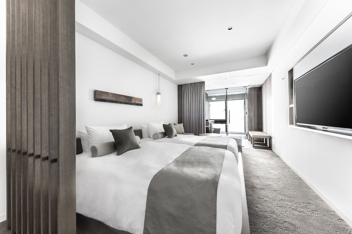 A hotel room with two beds, a large window, and a view of the outdoors.