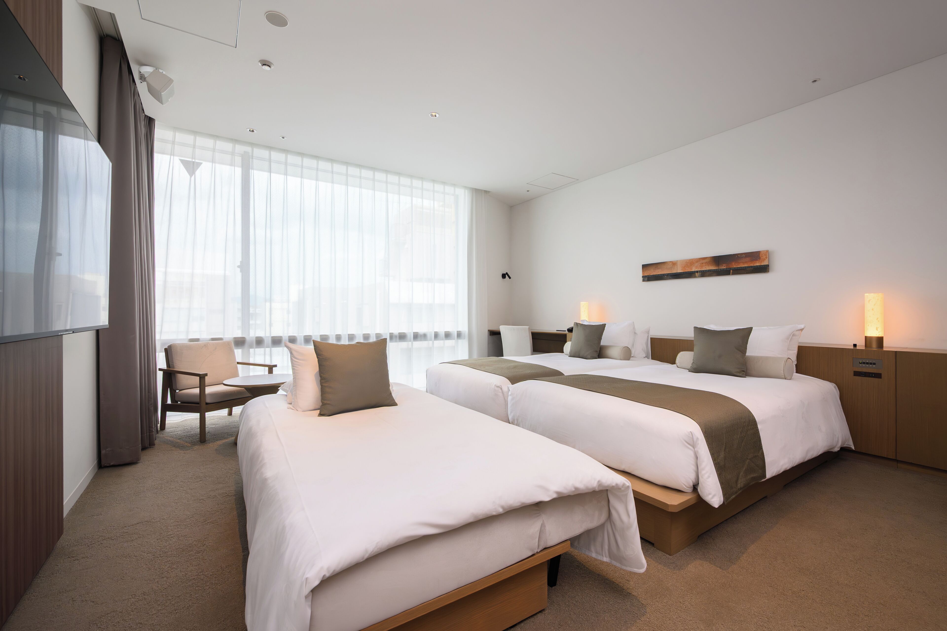 A hotel room with two beds, a desk, and a chair.