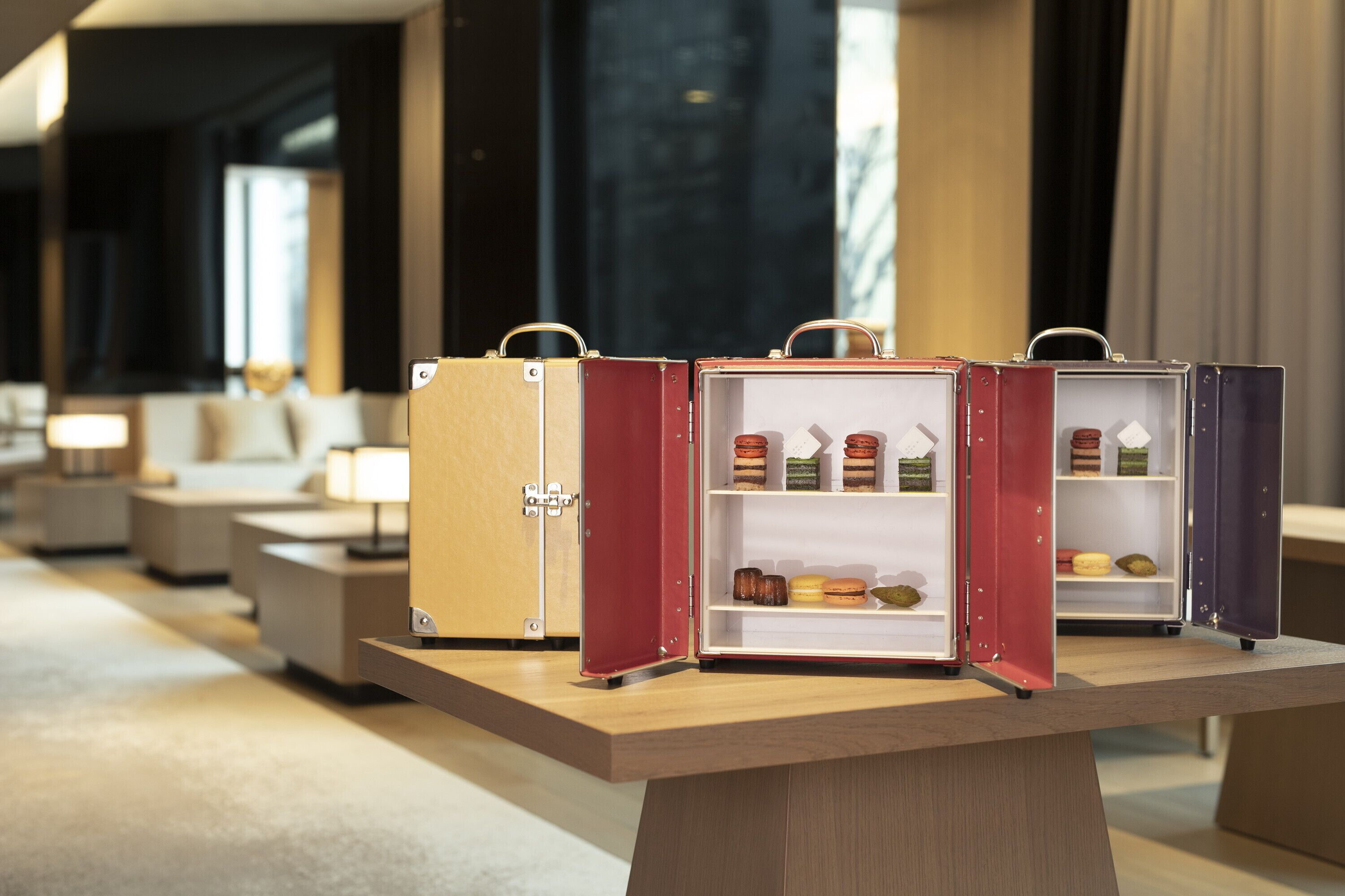 A display of vintage suitcases with compartments containing various items, placed on a wooden table in a modern hotel lobby.