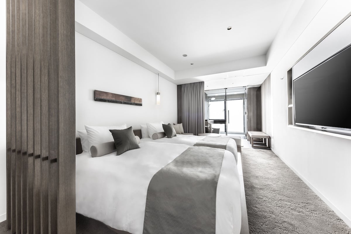 A hotel room with two beds, a large TV, and a view of the outdoors.