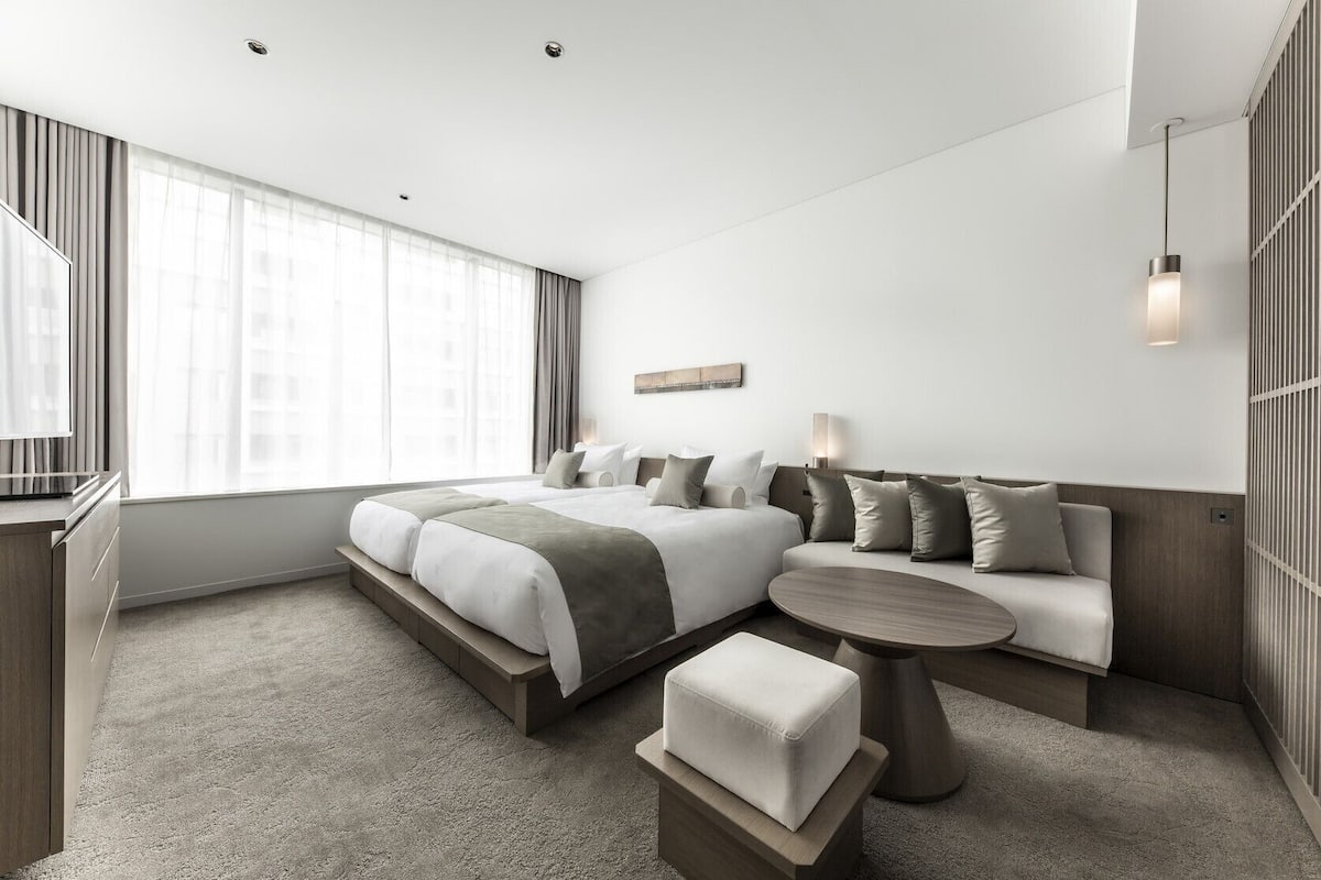 A modern hotel room with a large bed, a sofa, a small table, and a TV.