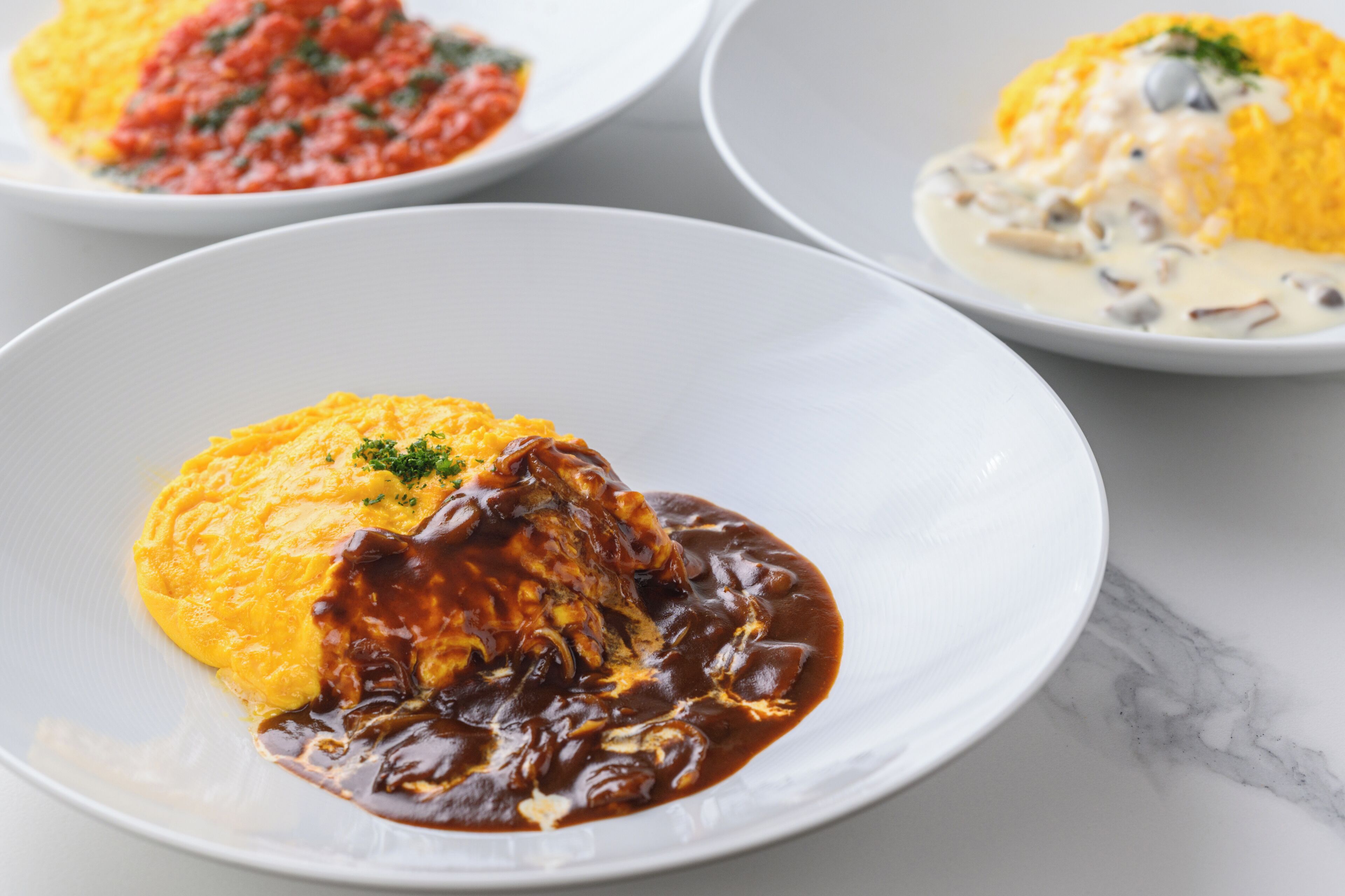 A plate of food with a yellow base and a dark sauce, and another plate with a similar dish but with a white base and a creamy sauce.