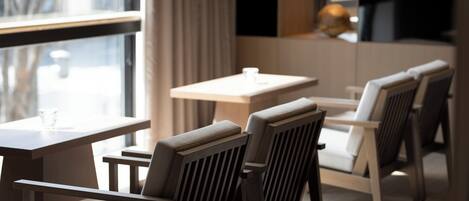 Un comedor moderno con mesas y sillas de madera, ventanas amplias con cortinas y una decoración minimalista.