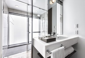 A modern bathroom with a large glass shower enclosure, a white sink, and a mirror.