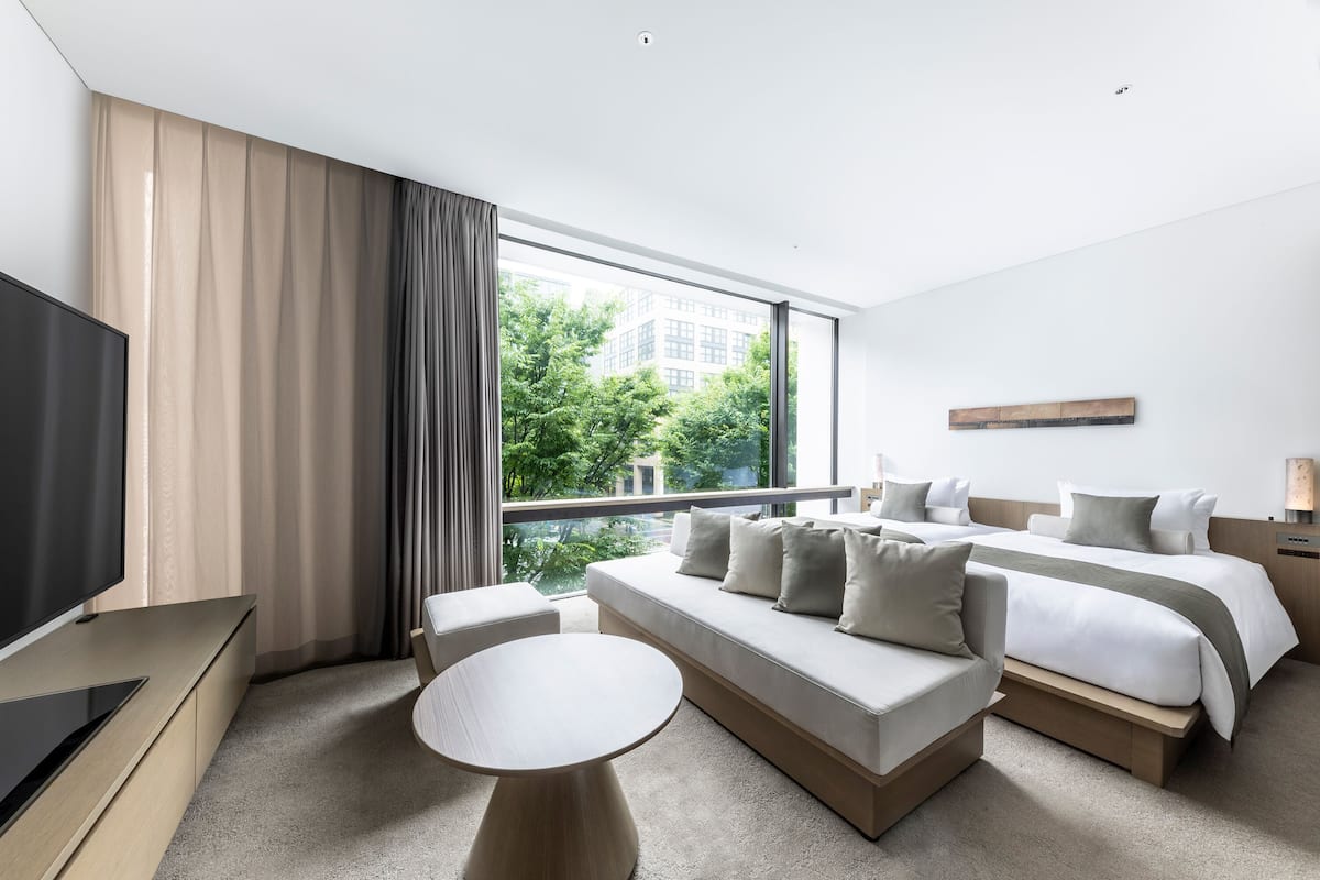 A modern hotel room with a large bed, a sofa, a TV, and a balcony with a city view.