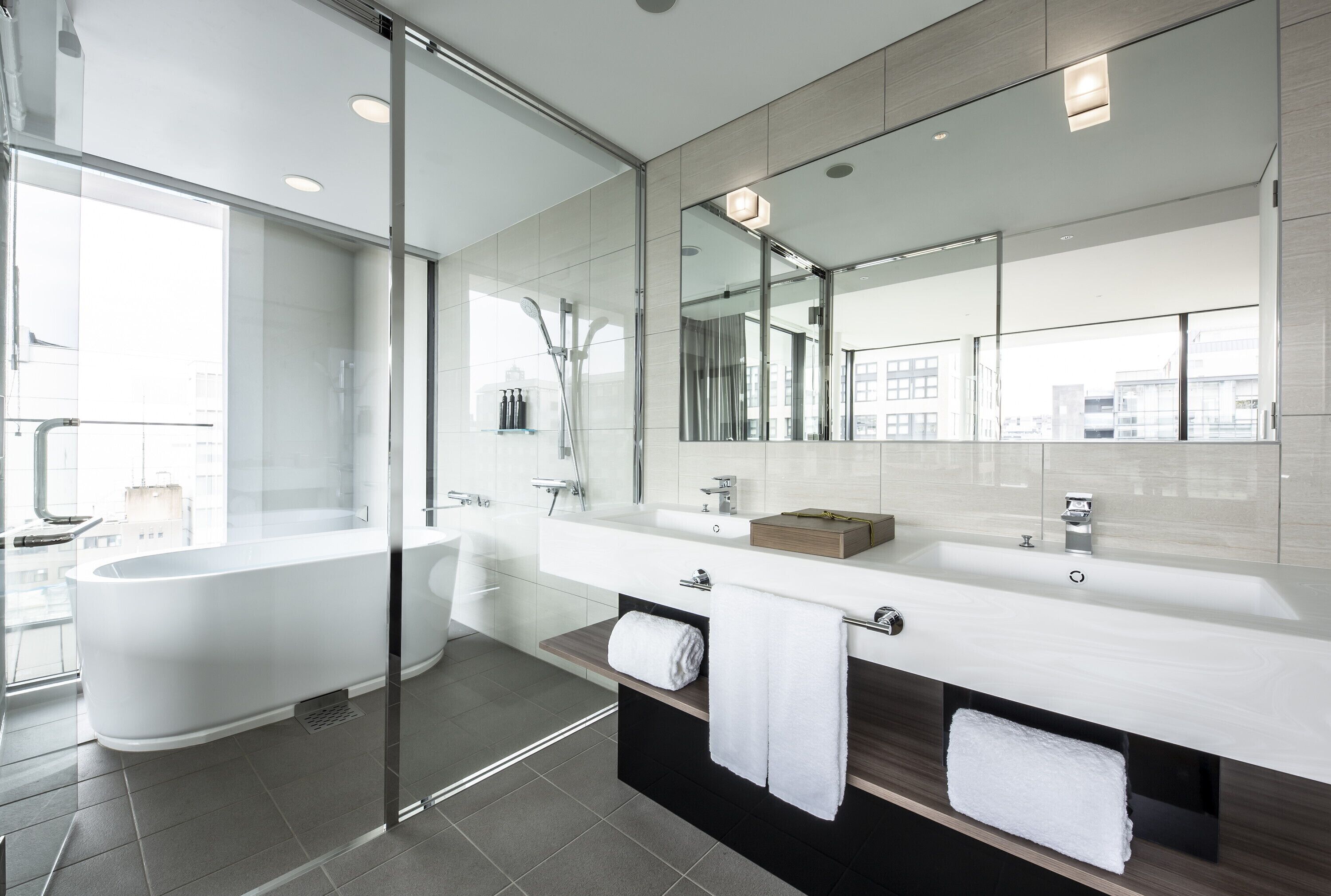Een moderne badkamer met een douche met glazen wand, een vrijstaand bad en een grote spiegel boven het wastafelmeubel.