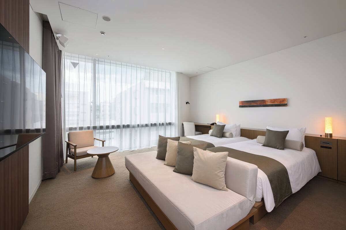 A modern hotel room with a large bed, a sofa, a small table, and a TV.