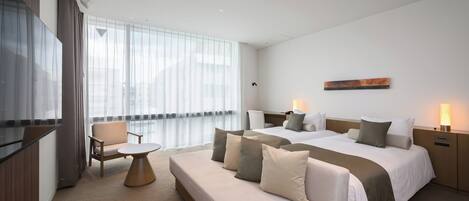 Una habitación de hotel moderna con una cama grande, un sofá, una mesita y un televisor.