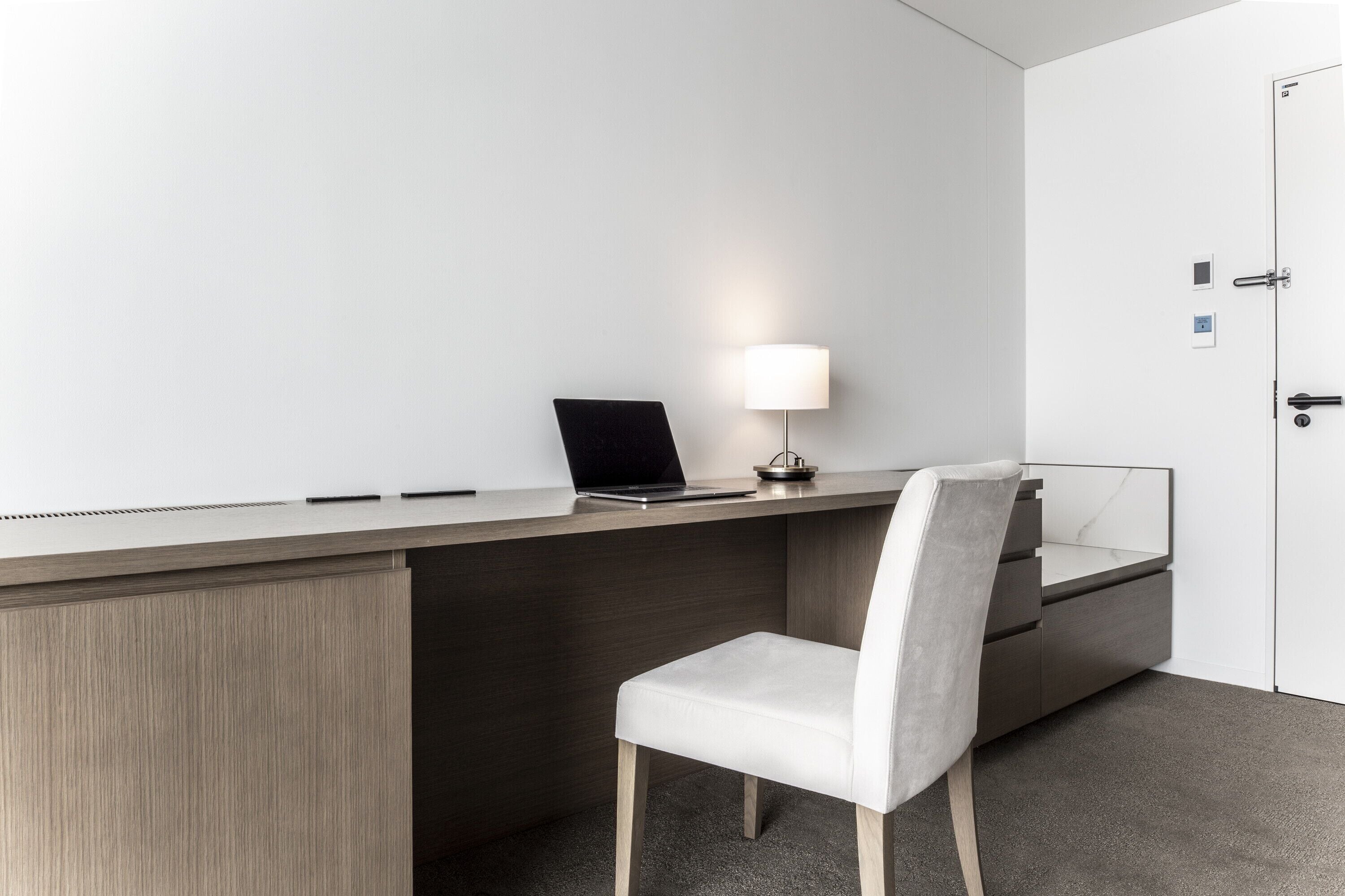 Un escritorio moderno con una computadora portátil, una lámpara y una silla.