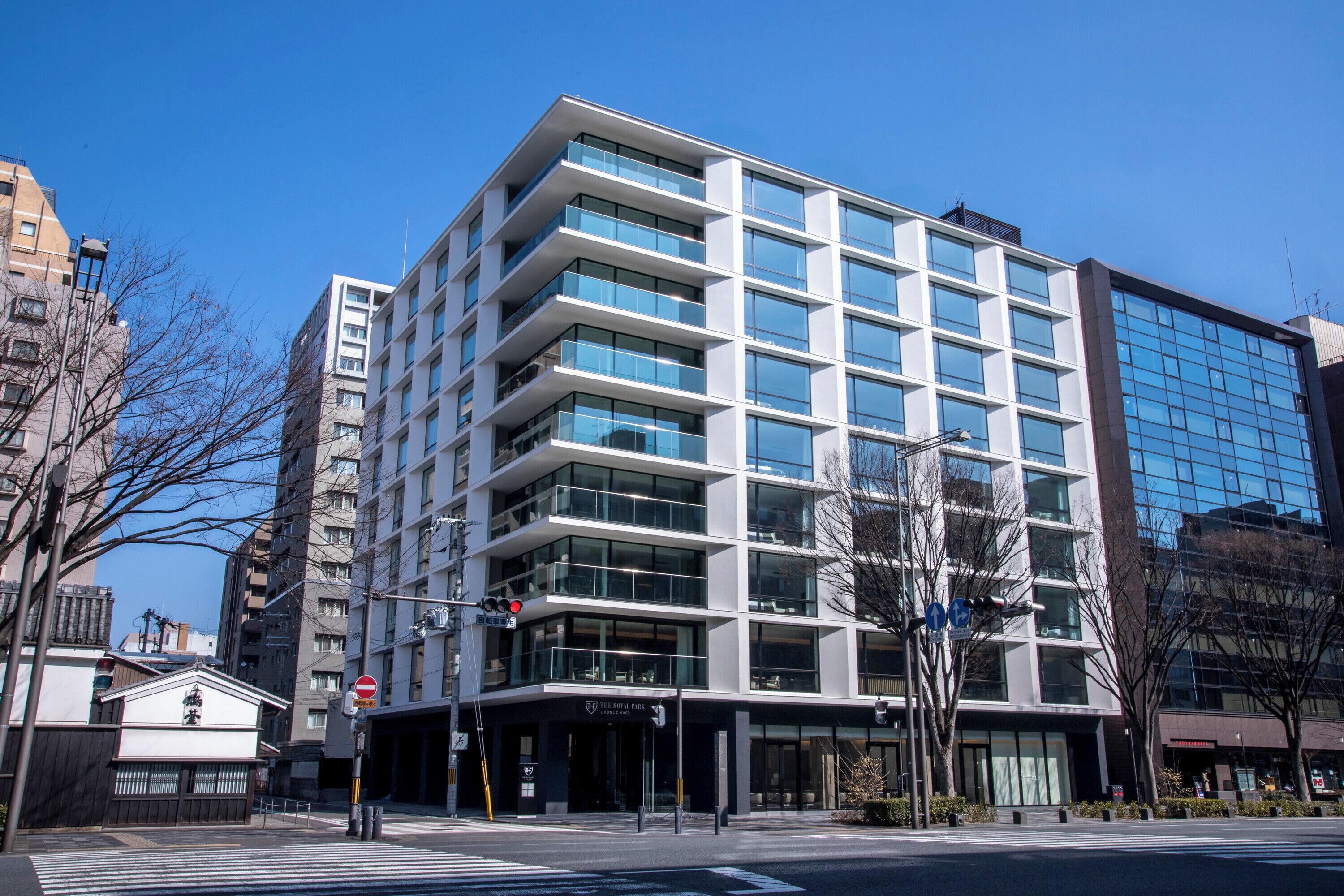 A modern multi-story building with a glass facade, a visible entrance, and a clear sky.