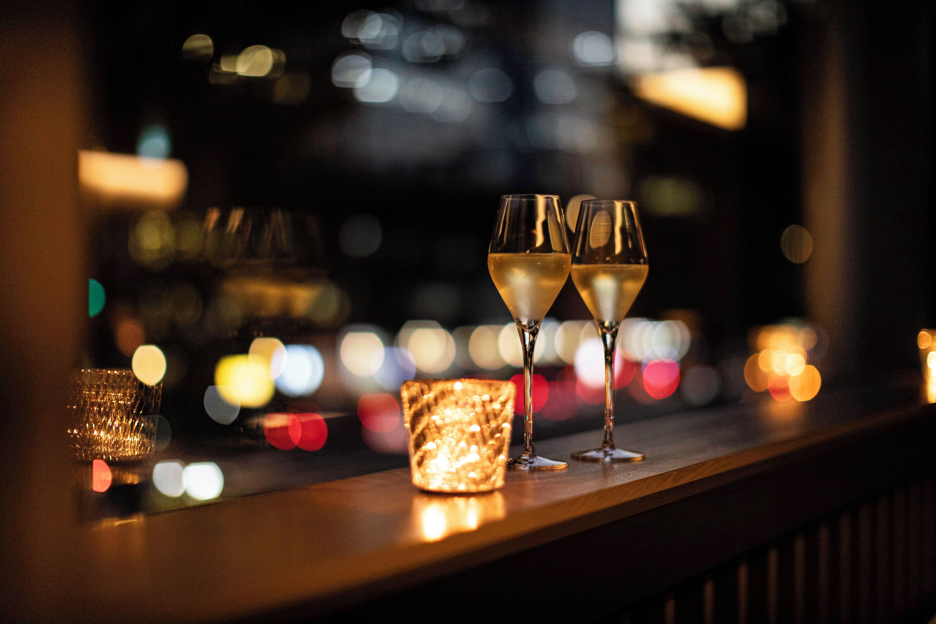Two glasses of champagne on a bar counter with a lit candle in the background.