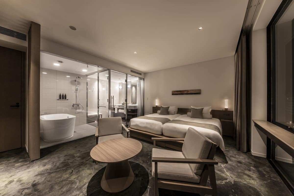 A modern hotel room with a large bed, a separate bathroom with a bathtub, a round table, and a sofa.
