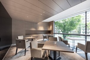 A modern dining area with wooden tables and chairs, large windows offering a view of the city.
