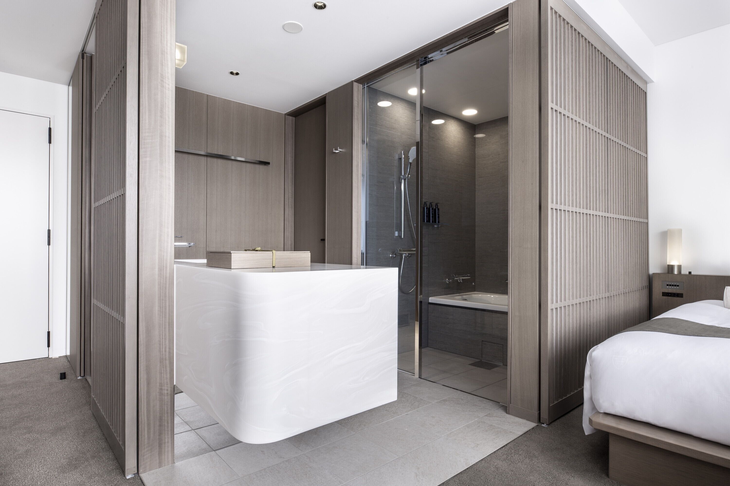 Una habitación de hotel moderna con una cama grande, un baño independiente con ducha de vidrio y tocador integrado.