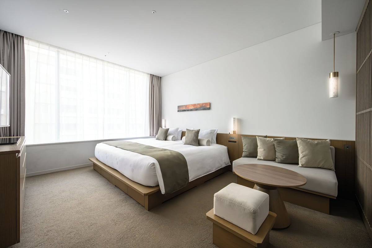 A modern hotel room with a large bed, a sofa, a small table, and a desk.
