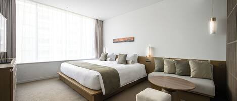 A modern hotel room with a large bed, a sofa, a small table, and a desk.