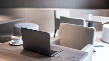 Un espacio lounge moderno con una laptop sobre una mesa de madera, una taza de café y asientos contemporáneos.