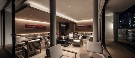 A modern hotel lobby with a spacious seating area, a fireplace, and a view of the city at night.