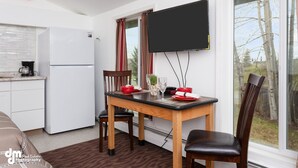 Una cocina compacta con un refrigerador blanco, una mesa de comedor con sillas y un televisor de pantalla plana montado en la pared.