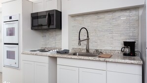 Una cocina moderna con armarios blancos, un lavamanos de acero inoxidable, un microondas negro y una cafetera.