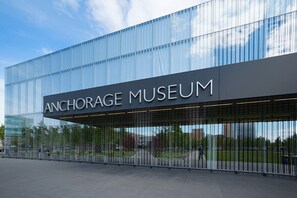 The exterior of the Anchorage Museum with a modern glass facade and a clear sky in the background.