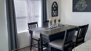 A dining room with a dark wooden table, grey curtains, and a chandelier.