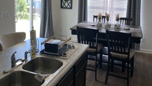 A modern kitchen with a central island, a dining area with a table and chairs, and a large window with curtains.