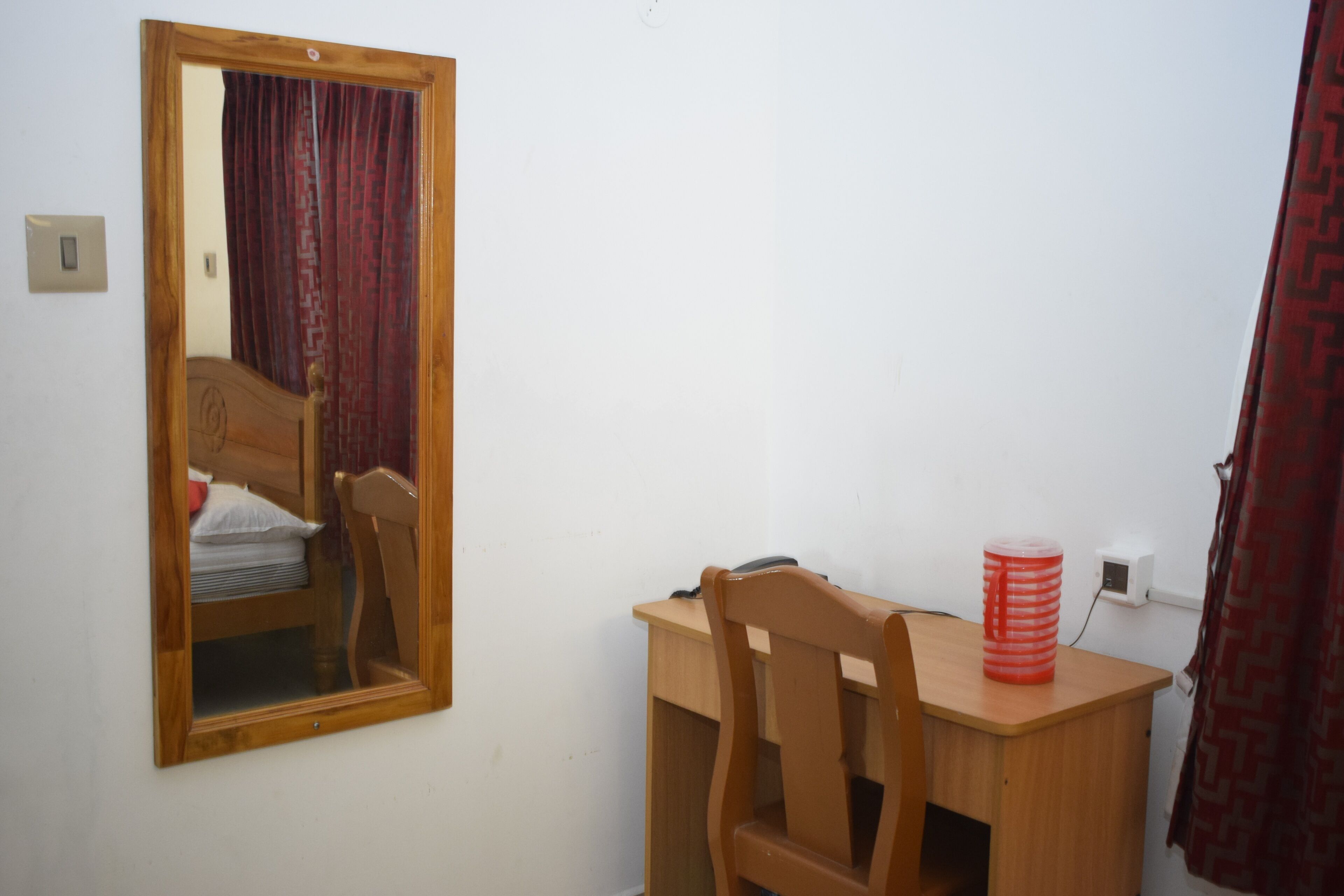 Une pièce comprenant un bureau en bois, une chaise, un miroir et un objet cylindrique rouge posé sur le bureau.