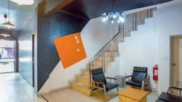 Ein modernes Interieur mit einer Treppe, zwei schwarzen Stühlen, einem Holztisch und einem hängenden, orangefarbenen Schild.