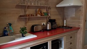 A kitchen with wooden cabinets, a red countertop, and a built-in oven. There are shelves above the counter holding various kitchen items. - Chez_vanilles_des_isles (L'Isle-sur-la-Sorgue)