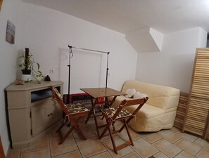 A small, cozy room with a wooden table and chairs, a sofa, a cabinet, and a plant.