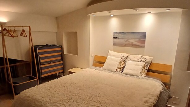 A bedroom with a large bed, a wooden headboard, a wall-mounted picture, and a hanging coat rack. - Chez_vanilles_des_isles (L'Isle-sur-la-Sorgue)