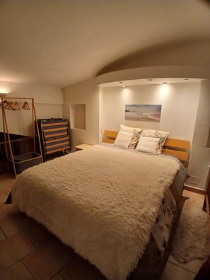 A bedroom with a large bed, a wooden headboard, a wall-mounted picture, and a hanging coat rack. - Chez_vanilles_des_isles (L'Isle-sur-la-Sorgue)