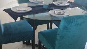 Comedor con una mesa de vidrio, seis sillas color turquesa y una camino de mesa negra.