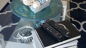 Una sala de estar con un sofá, una mesa de centro de vidrio y una pila de libros.