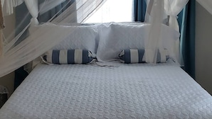 Una cama con colcha blanca, almohadas a rayas azules y blancas, y cortinas de dosel blancas.