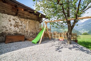 Un espace de jeux rustique en bois, avec un toboggan vert, une balançoire en bois et un arbre.