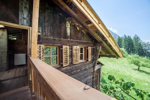 A wooden cabin with a balcony, a stone wall, and a view of a forest.