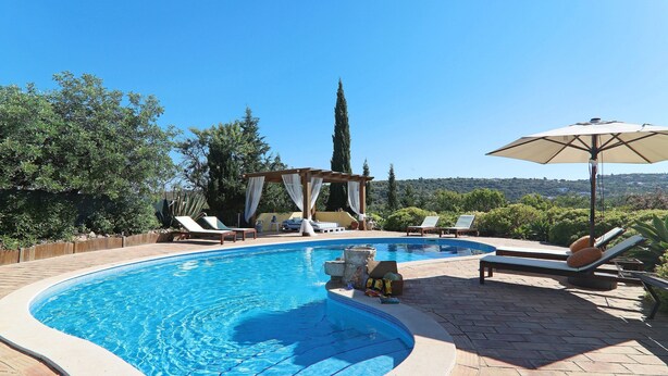 Una piscina con pérgola, sillas de descanso y una sombrilla.