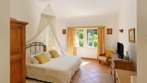 Un dormitorio con cama, una silla, un escritorio, una ventana y cortinas.